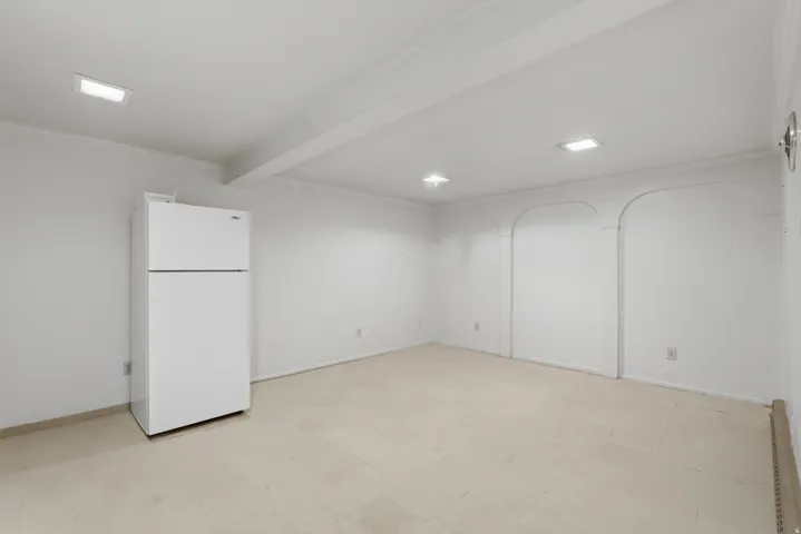 Recessed lighting fixtures illuminate the space, featuring a top-freezer refrigerator and arched wall detailing