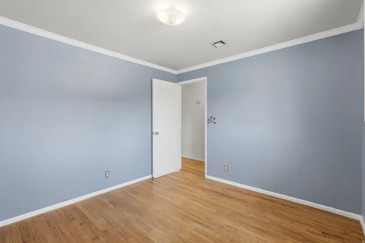 Wood-finish flooring, white crown molding, ceiling-mounted light fixture, and a white interior door