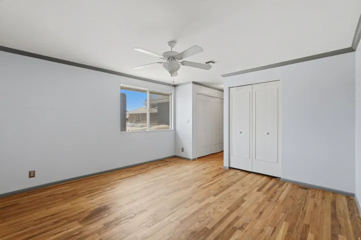 Wood-finish flooring, white walls, white ceiling fan, and white bi-fold closet doors