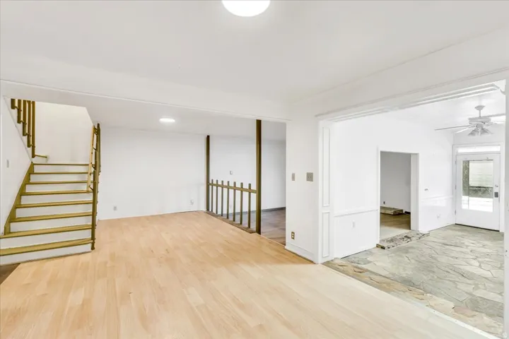 Wood-finish flooring, staircase with wood railings, stone flooring, decorative trim, and ceiling fan with light fixture