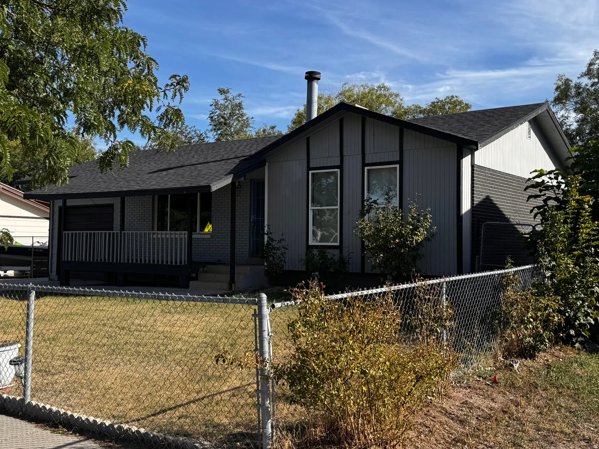 Gable roofline with asphalt shingles, featuring a covered porch with railing, exterior siding, and a chain-link fence