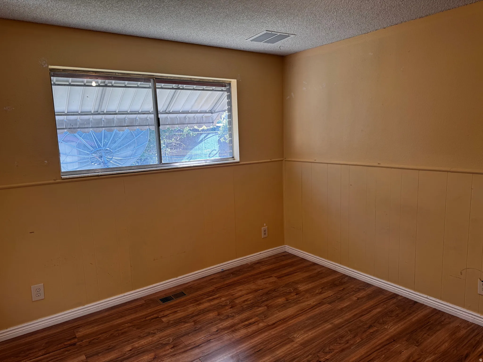 Wood-finish flooring with white trim, a single window, and textured ceiling