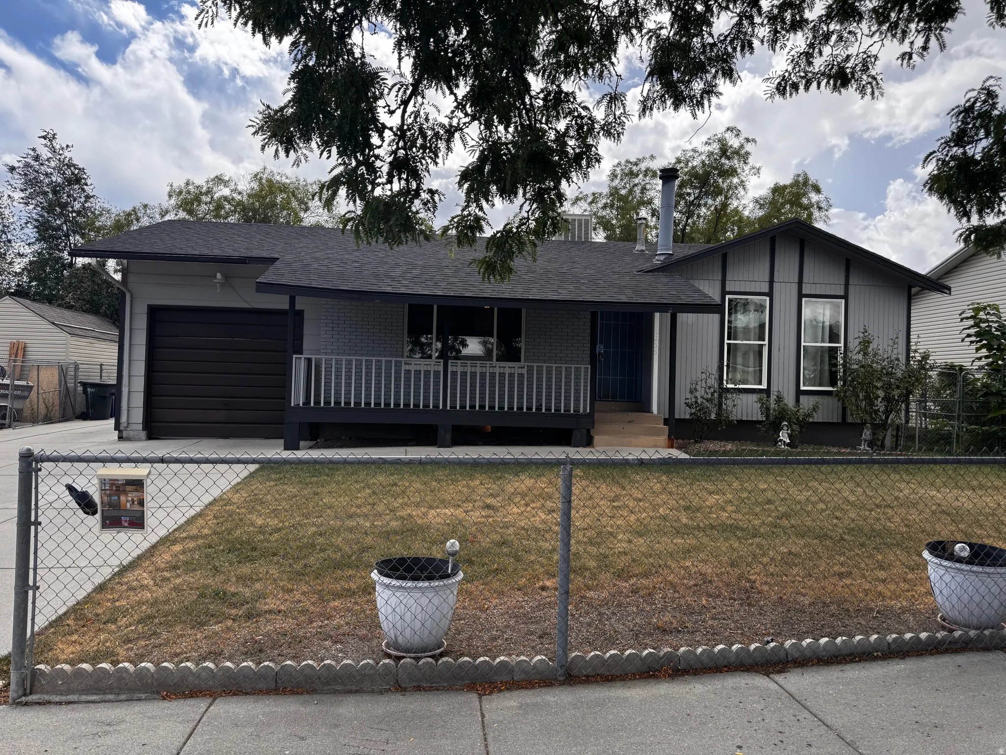 Front exterior featuring a covered porch with railing, attached garage, and a chain-link fence