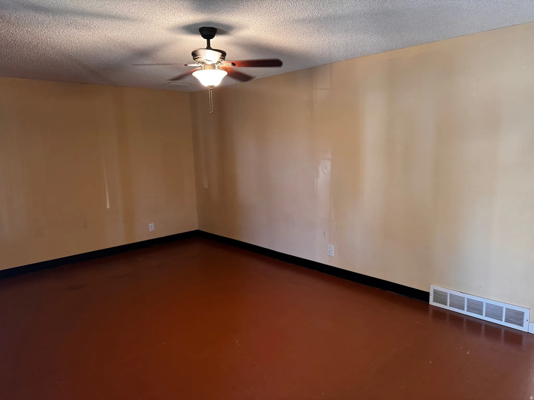 Ceiling fan with integrated lighting, textured ceiling, light-toned walls, dark trim, and reddish-brown flooring