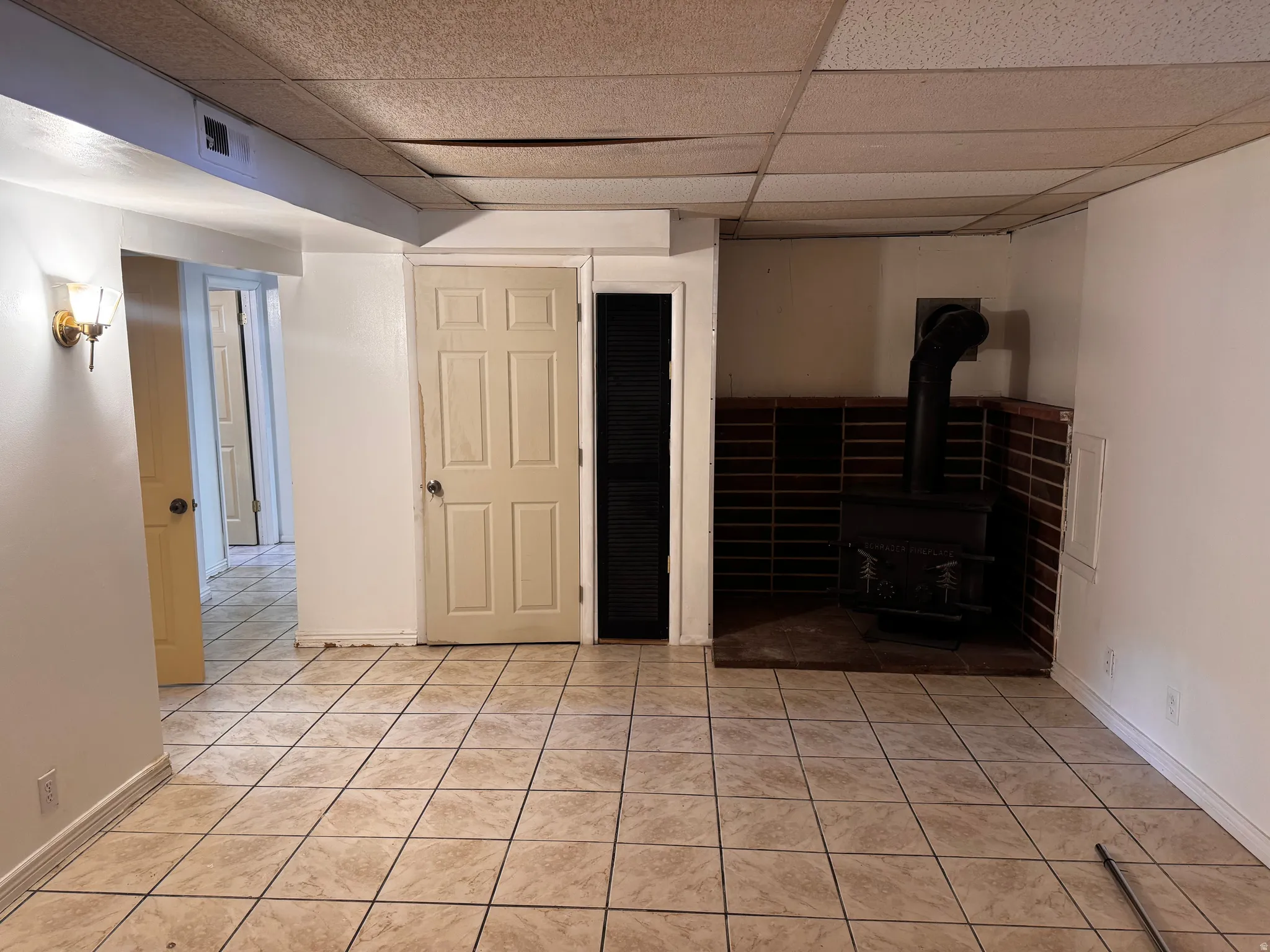 Tiled flooring, wood-burning stove with brick surround, wall-mounted light fixture, paneled doors, and painted walls
