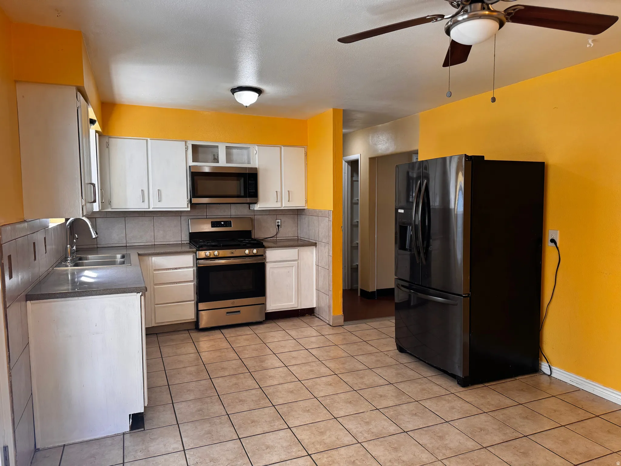 Kitchen featuring tile flooring, white cabinetry, stainless steel appliances, a ceiling fan, and a built-in microwave