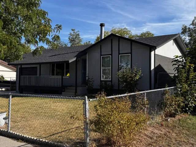 Gable roofline with asphalt shingles, featuring a covered porch with railing, exterior siding, and a chain-link fence