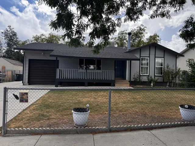 Front exterior featuring a covered porch with railing, attached garage, and a chain-link fence