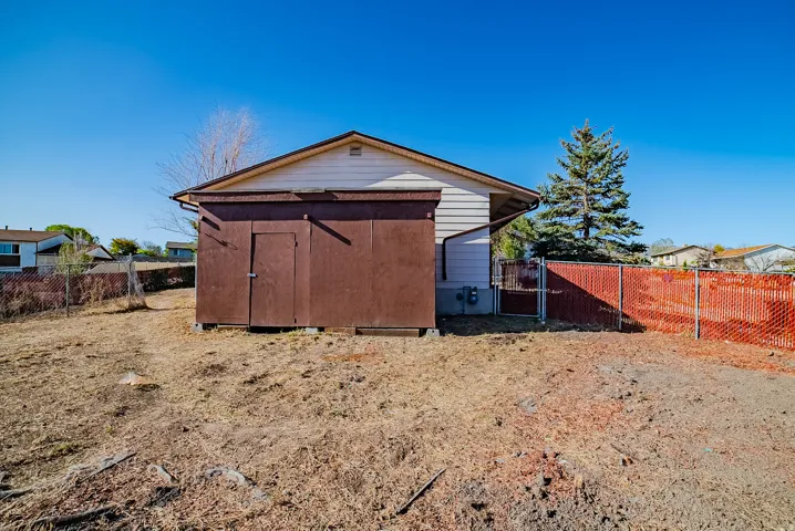 Detached storage shed with a single entry door and an adjacent chain-link fence