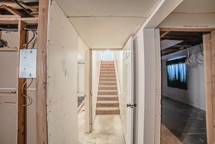 Unfinished interior spaces featuring exposed framing, electrical conduit, partial drywall installation, and a carpeted staircase