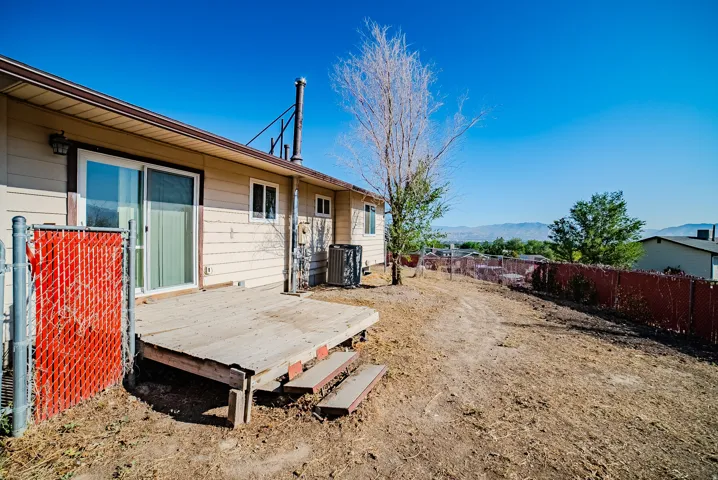 Rear exterior with sliding glass door access to a wood deck, chain link fencing, and distant mountain scenery