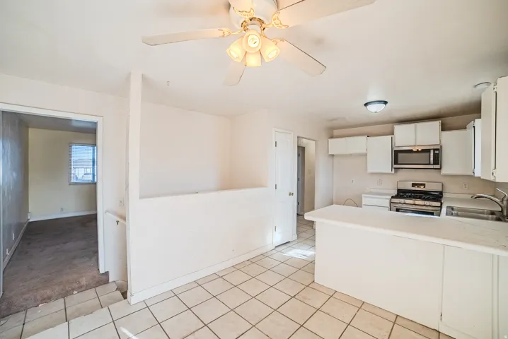 Kitchen featuring white cabinetry, stainless steel microwave, gas range, and a white countertop