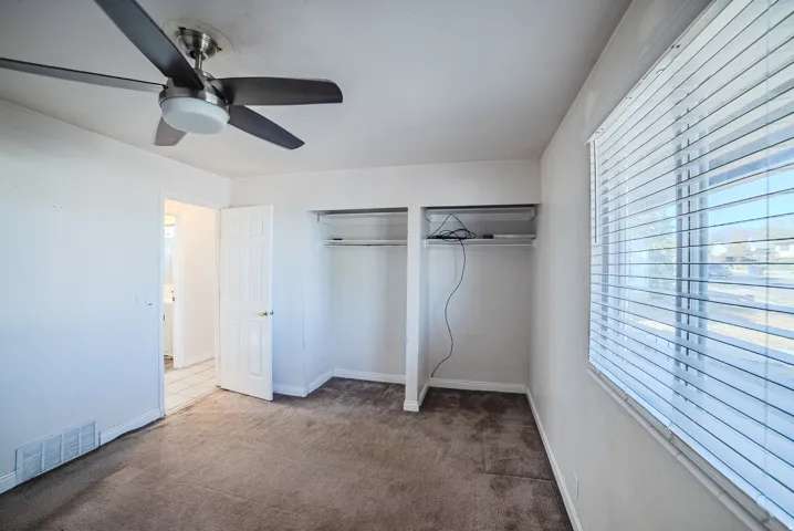 Carpeted room with a ceiling fan, built-in closet storage, and window blinds