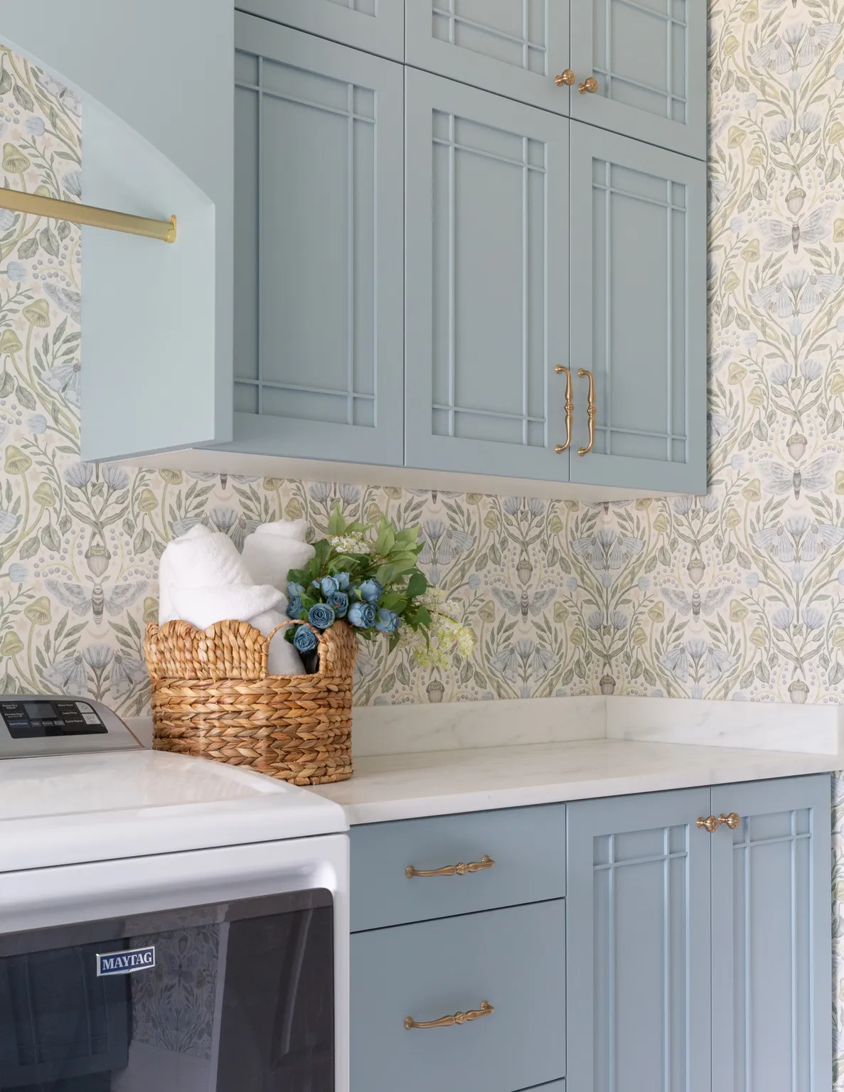 Custom cabinetry with decorative molding and brass hardware, complemented by a solid surface countertop, and botanical print wallpaper