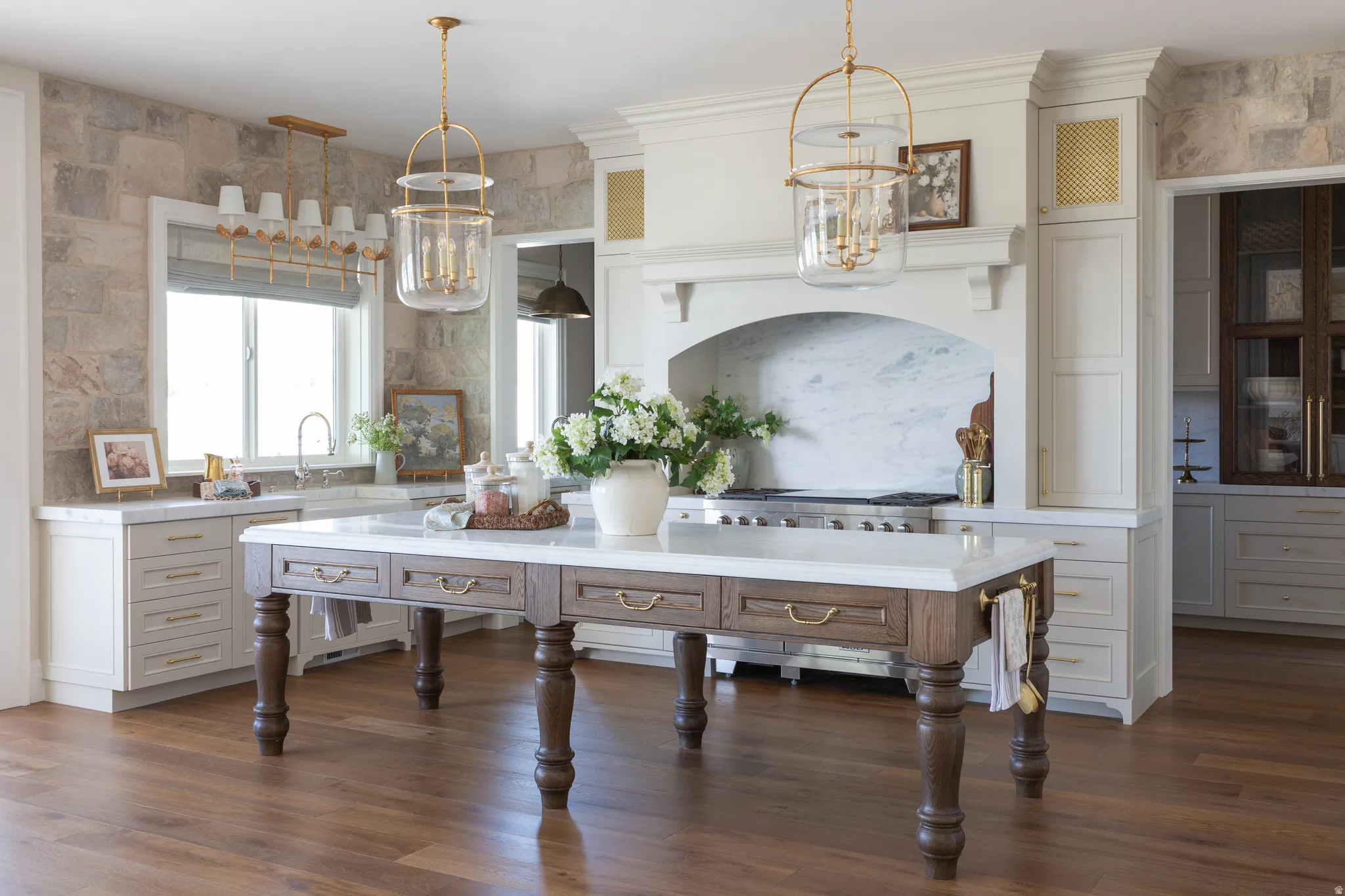 Expansive kitchen featuring a marble-topped island, light wood-finish flooring, custom cabinetry, a built-in range hood with marble backsplash, and dual pendant lighting