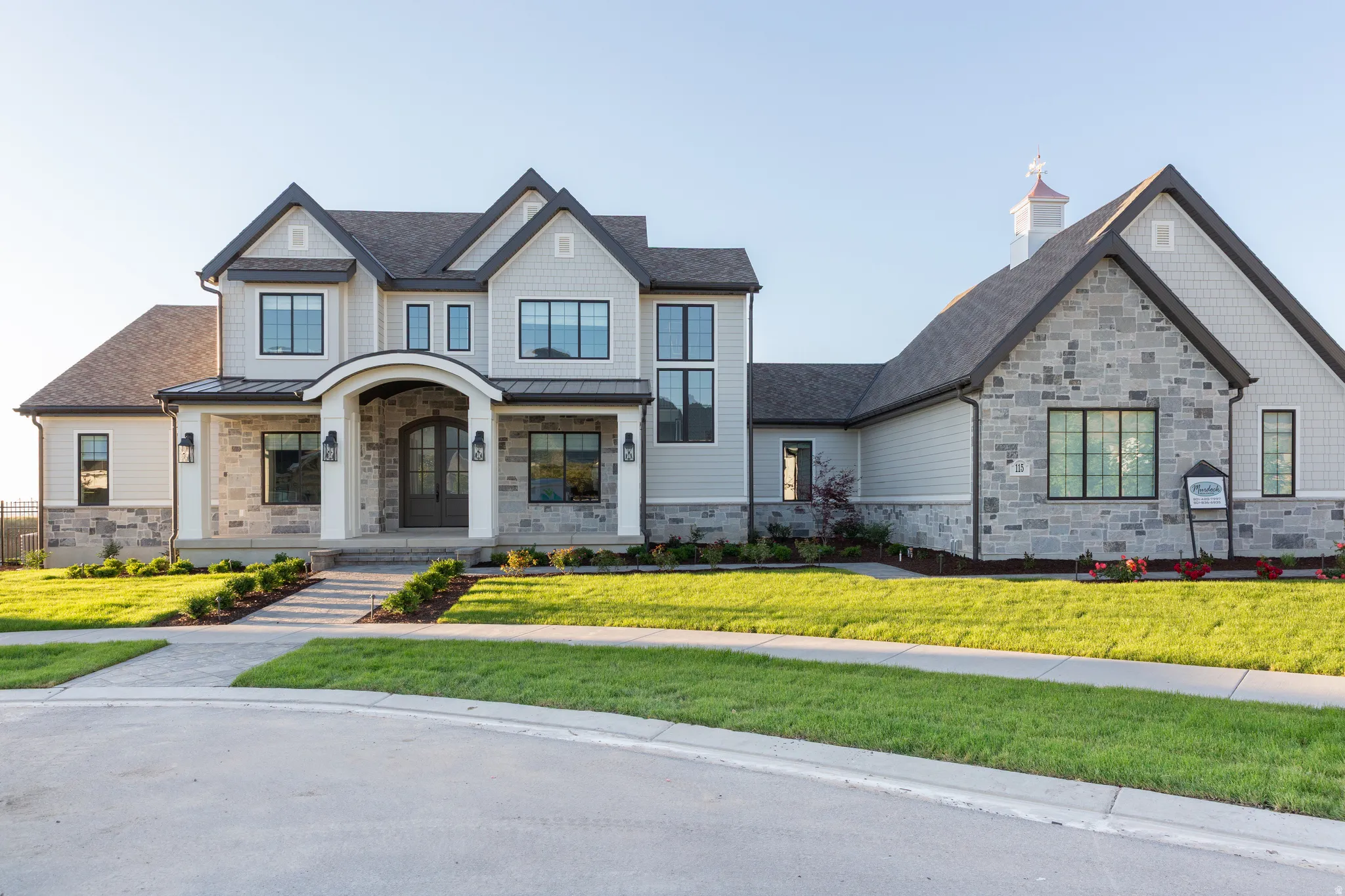 Stone and siding exterior with dark-framed windows, a covered entry, and a cupola accent