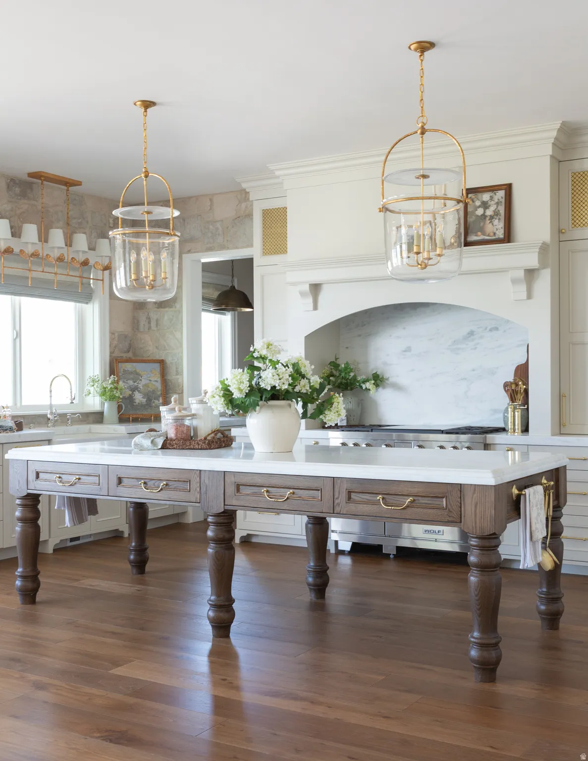 Kitchen featuring a substantial island with integrated drawers, wood-finish flooring, stone countertops, a decorative range hood, and pendant lighting