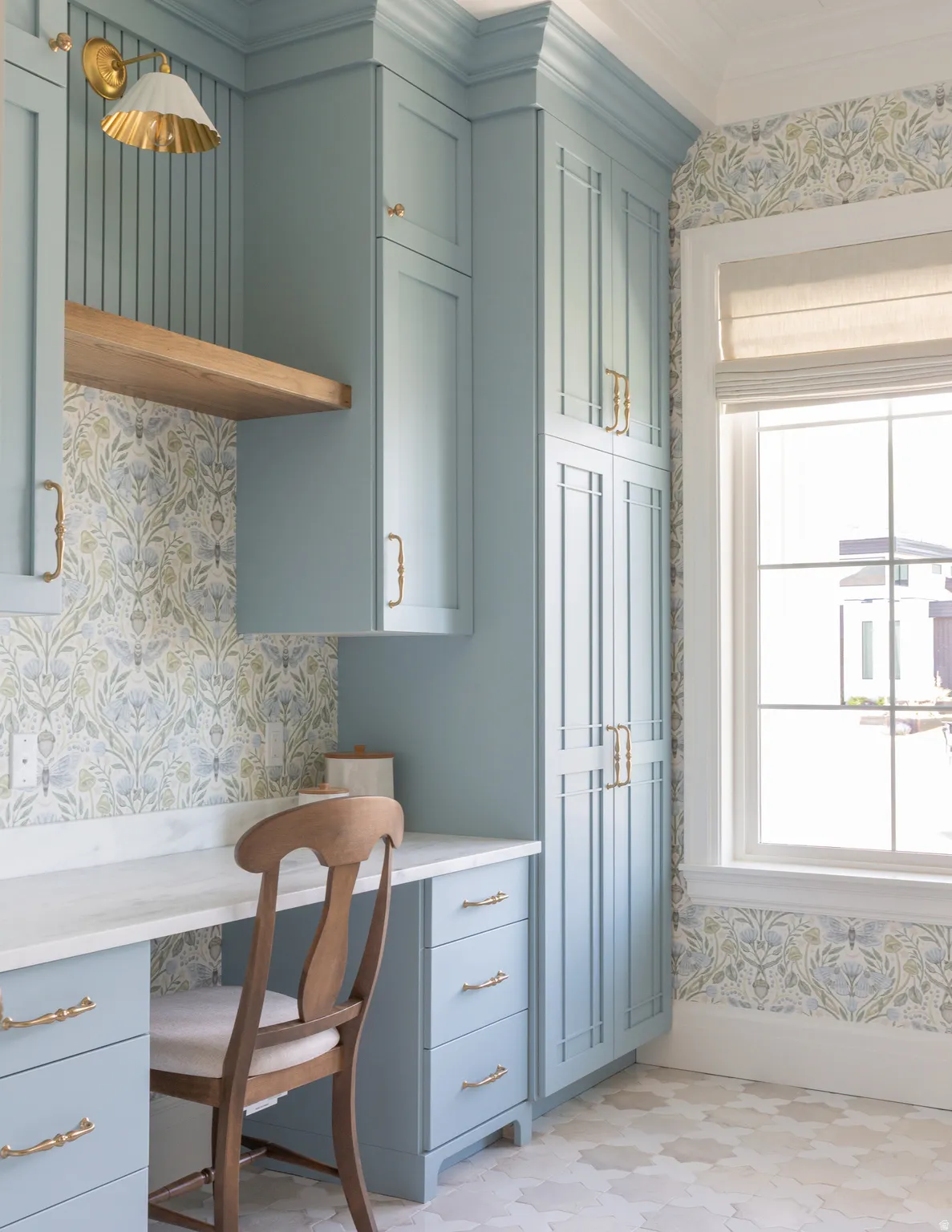 Built-in cabinetry with crown molding, integrated desk area with stone countertop, wood-finish floating shelf, and hexagonal floor tile