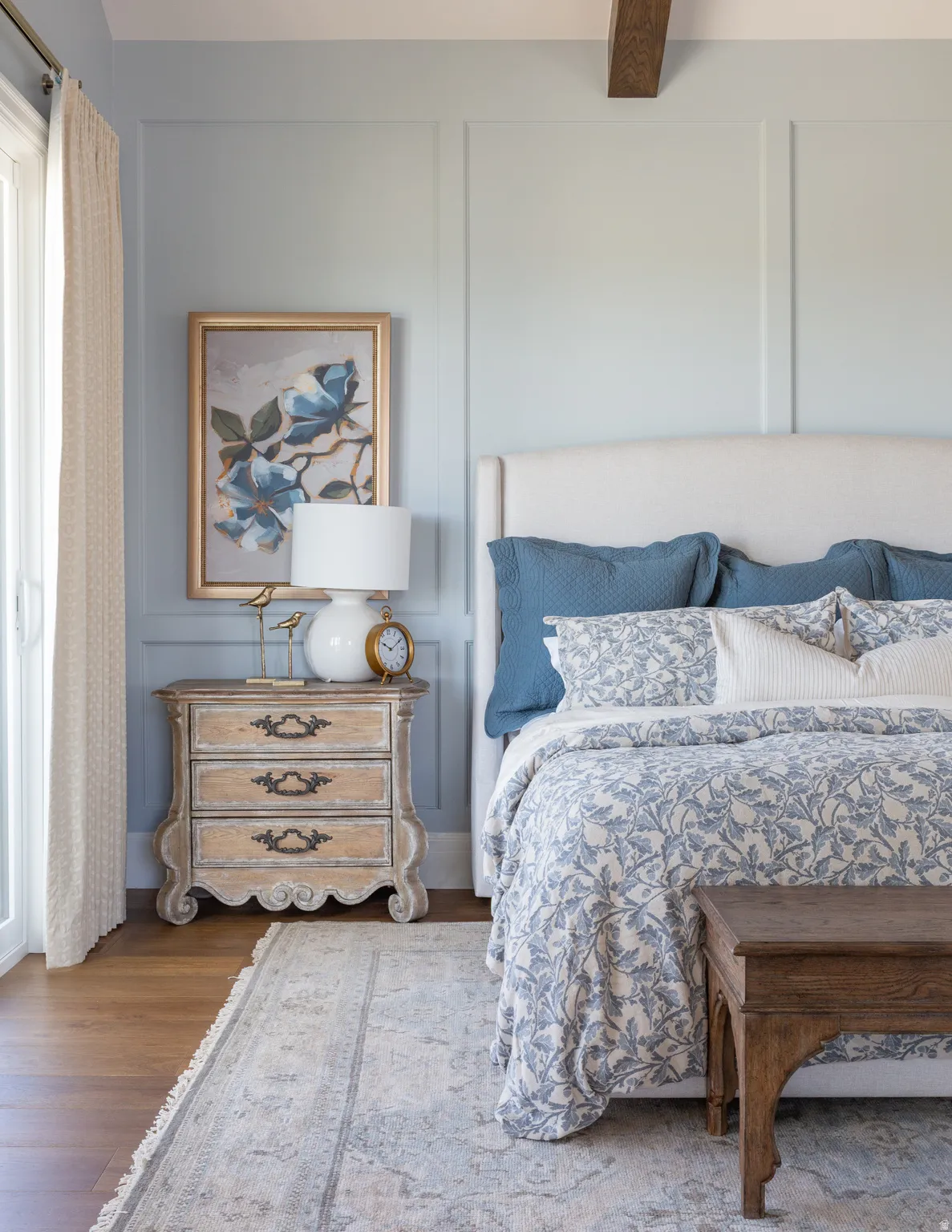 Board and batten wall paneling, upholstered headboard, wood-finish flooring, exposed ceiling beam, and a full-light glass door