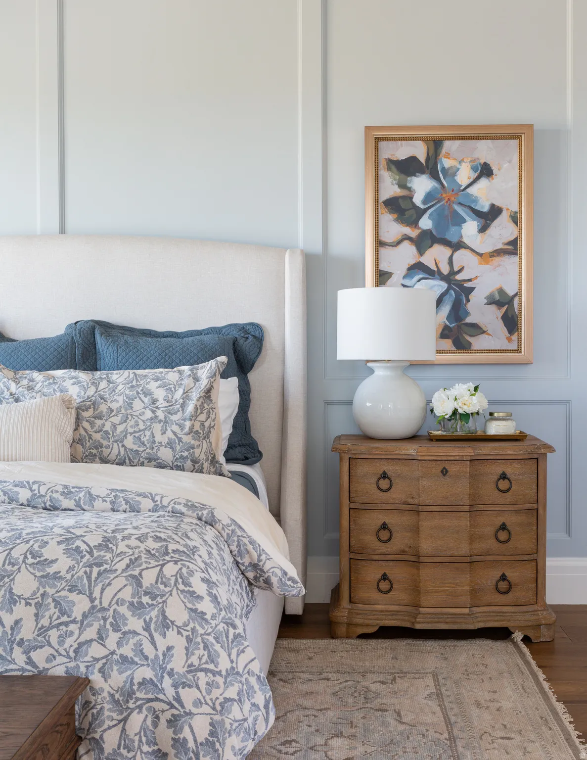 Wainscoting wall paneling, light wood-finish flooring, and a decorative nightstand with ring pull hardware