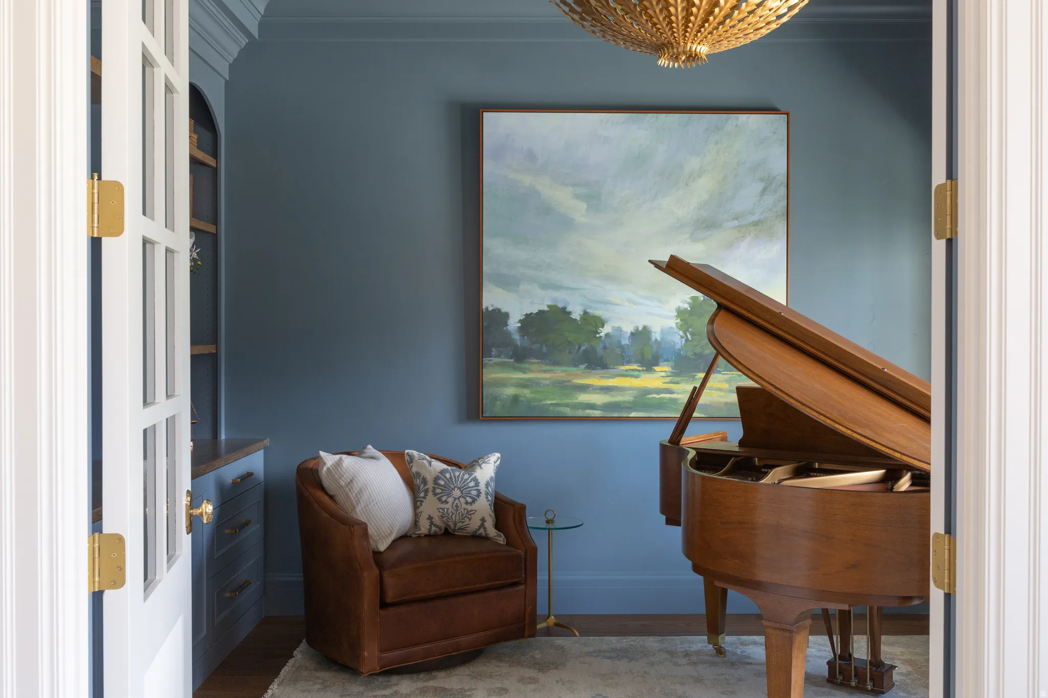 French doors with brass hardware opening to a room with built-in cabinetry, a decorative ceiling fixture, and deep-toned walls