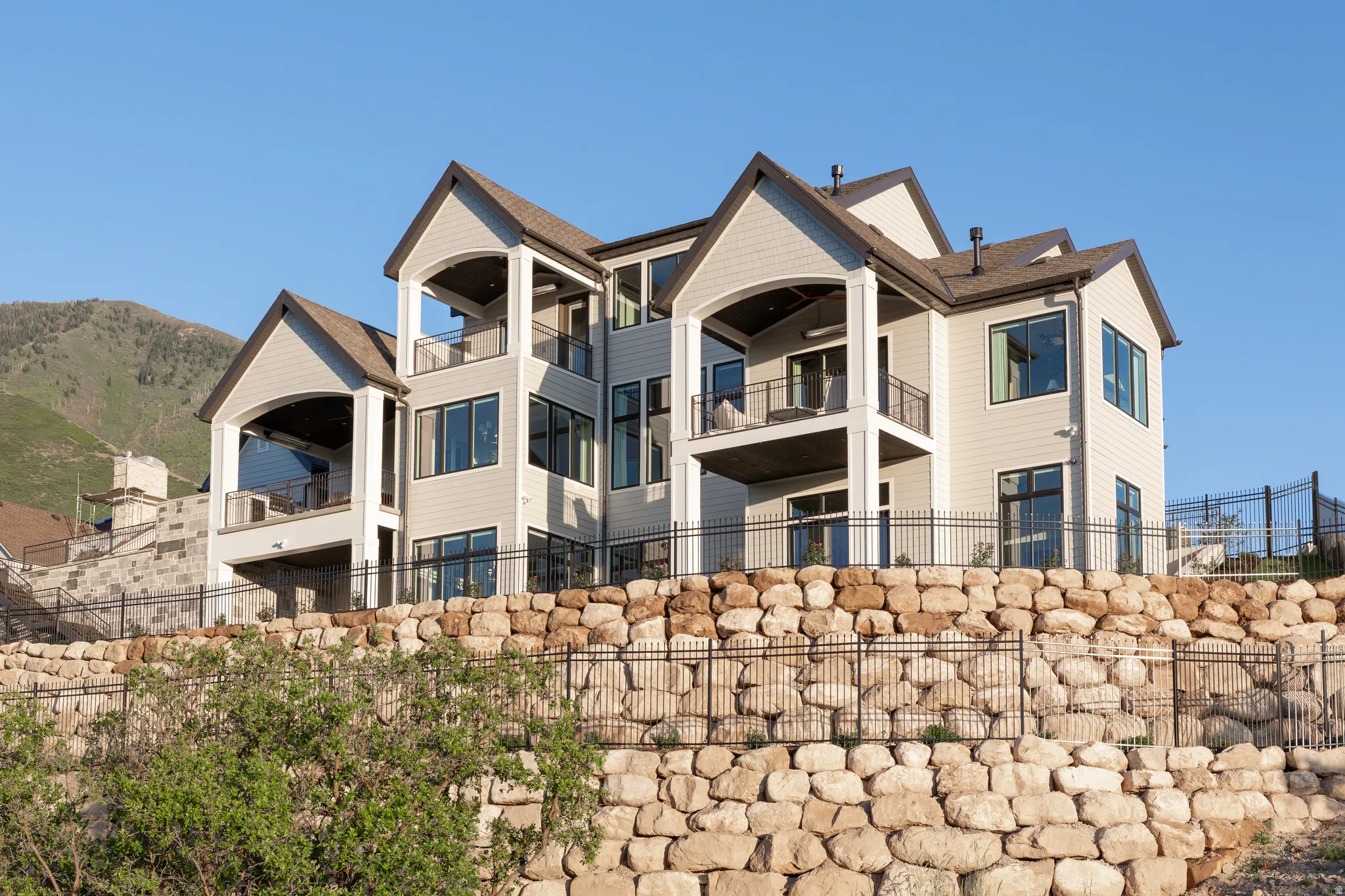 Multi-level residence featuring light-colored siding, multiple balconies, and a stone retaining wall