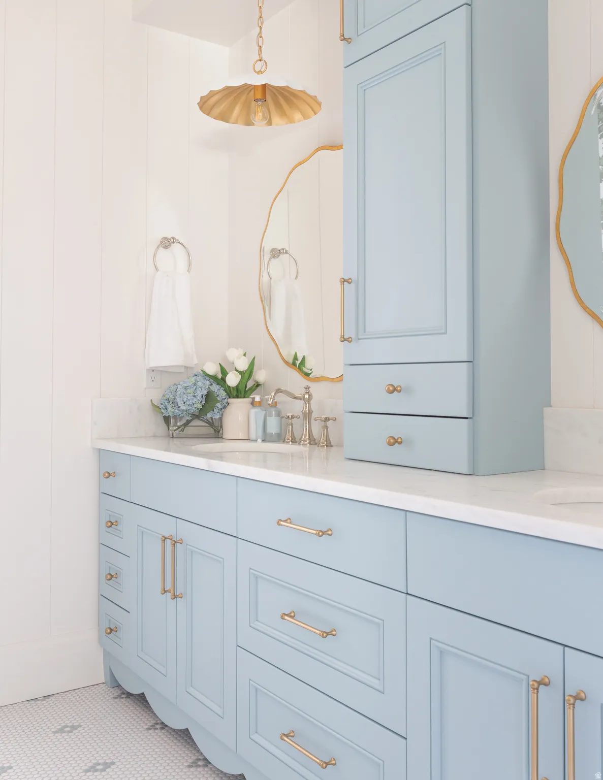 Light blue cabinetry with gold-tone hardware, white countertop, white vertical paneling, and an overhead pendant light