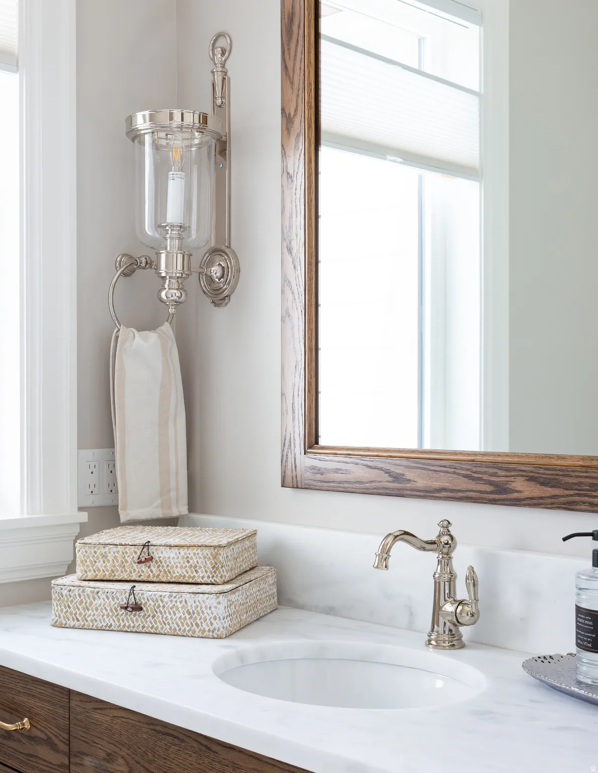 Vanity with a white countertop and integrated sink, a wood-framed mirror, and a polished nickel wall sconce