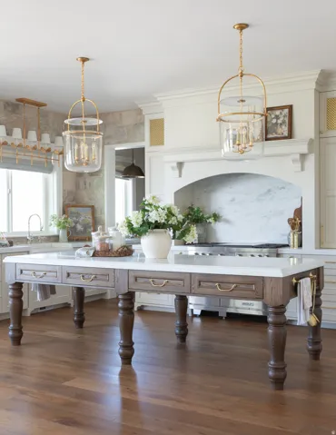 Kitchen featuring a substantial island with integrated drawers, wood-finish flooring, stone countertops, a decorative range hood, and pendant lighting