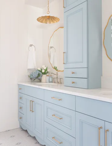 Light blue cabinetry with gold-tone hardware, white countertop, white vertical paneling, and an overhead pendant light