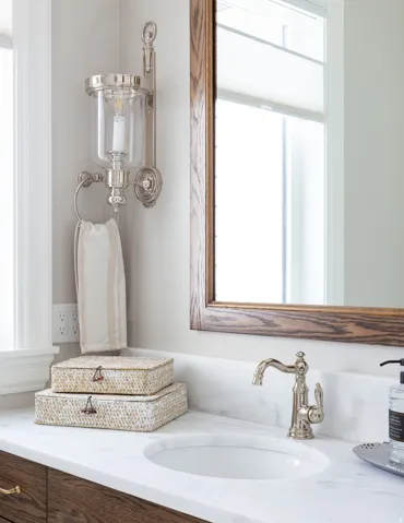 Vanity with a white countertop and integrated sink, a wood-framed mirror, and a polished nickel wall sconce