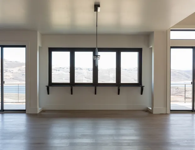 Expansive room featuring wood-finish flooring, a contemporary chandelier, multiple large windows with dark frames, a built-in window ledge, and sliding glass doors