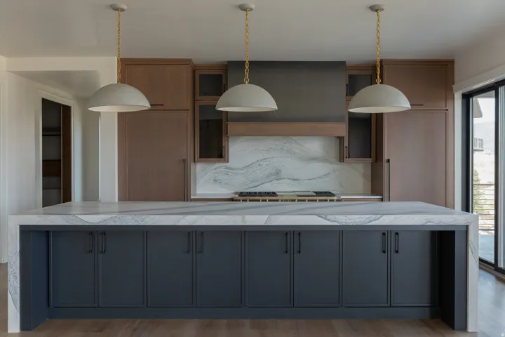 Kitchen featuring a large waterfall island, integrated appliances, natural wood cabinetry, a range hood, and pendant lighting
