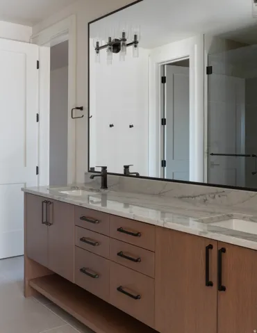 Dual vanity with stone countertop, integrated sinks, wood-finish cabinetry, and matte black hardware