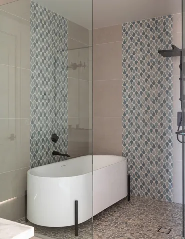 Freestanding soaking tub with matte black fixtures, glass-enclosed shower, pebble-finish shower floor, and decorative mosaic tile accents