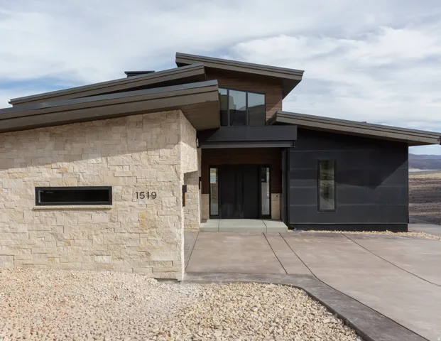 Modern architectural design featuring stacked stone, a dark paneled facade, and a flat roofline