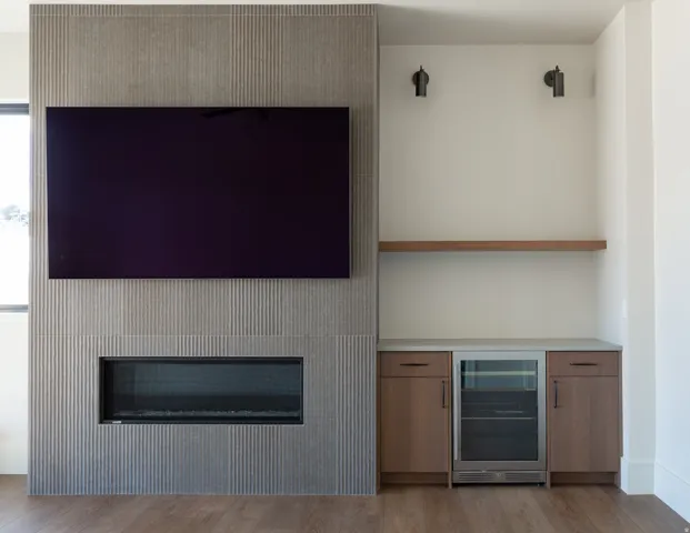 Recessed fireplace with textured surround, integrated beverage refrigerator, built-in cabinetry, and floating wood shelf
