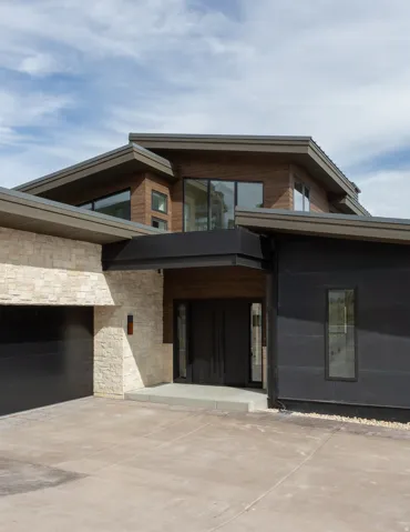 Modern exterior with mixed material siding, featuring natural stone accents, wood-finish panels, and dark siding
