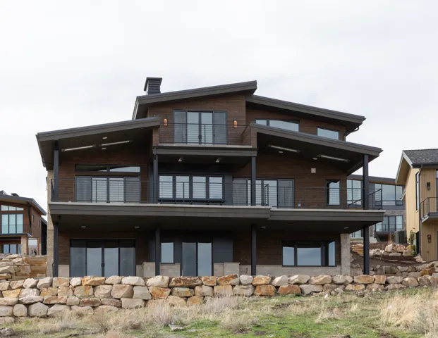 Multi-level contemporary exterior with dark wood-finish siding, multiple covered balconies, large windows, and a stone retaining wall