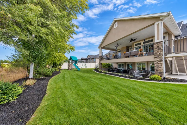 Expansive manicured lawn with mature trees, a multi-level deck, and a lower-level patio