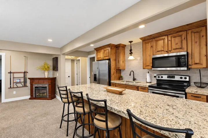 Kitchen featuring wood cabinetry, stainless steel appliances, a tiled backsplash, and an extended island with a solid surface countertop