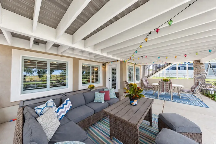 Expansive covered patio featuring a wood-beam ceiling, concrete flooring, and multiple windows with interior plantation shutters