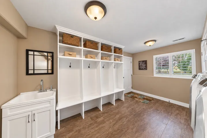 Built-in white cubby storage with upper shelving, wood-finish flooring, and a utility sink with cabinet storage