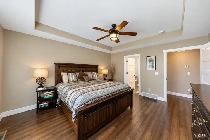 Tray ceiling with a ceiling fan, wood-finish flooring, and white trim
