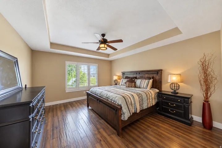 Tray ceiling with a ceiling fan, wood-finish flooring, and window shutters