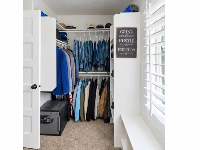 Walk-in closet with carpet flooring, built-in shelving, and a window with plantation shutters
