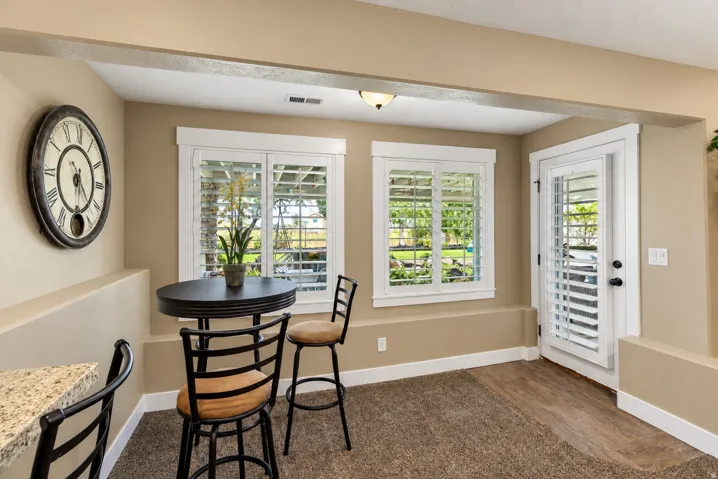 Carpet and wood-finish flooring, two windows with plantation shutters, a glass-paneled door with plantation shutters, and a built-in granite-finish countertop
