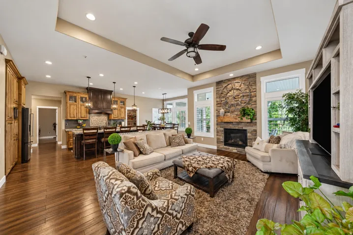 Stone-faced fireplace with a wood mantel, wood-finish flooring, recessed lighting, tray ceiling, and a built-in entertainment center