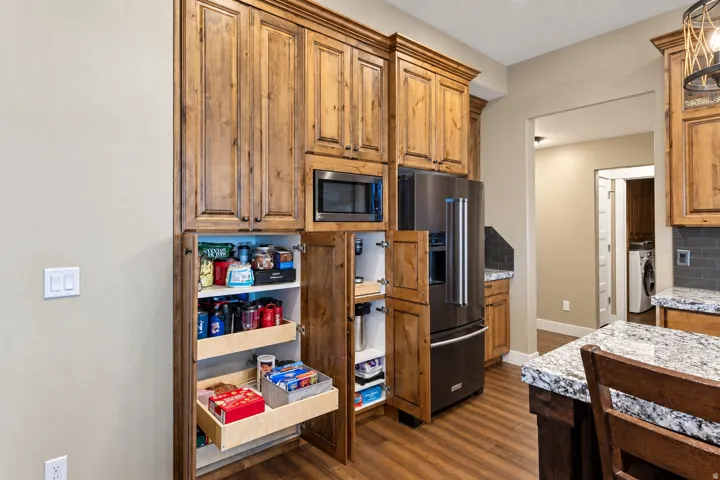 Wood-finish cabinetry with crown molding, stainless steel microwave, black stainless steel refrigerator, granite countertops, and wood-finish flooring
