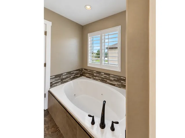 Jetted soaking tub with a tiled surround, framed by a window with plantation shutters